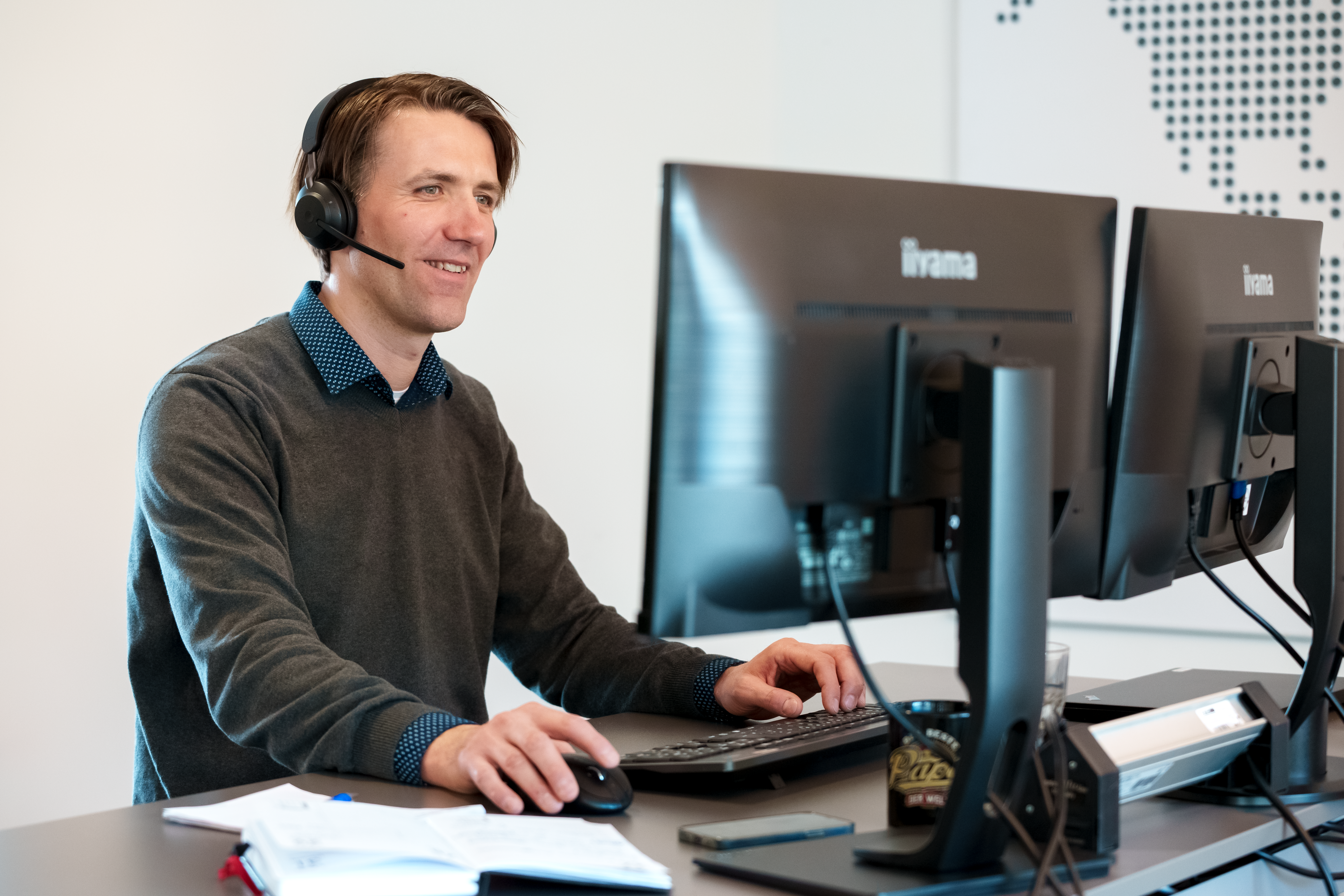 Man standing at his desk wearing a headset and looking at his computer