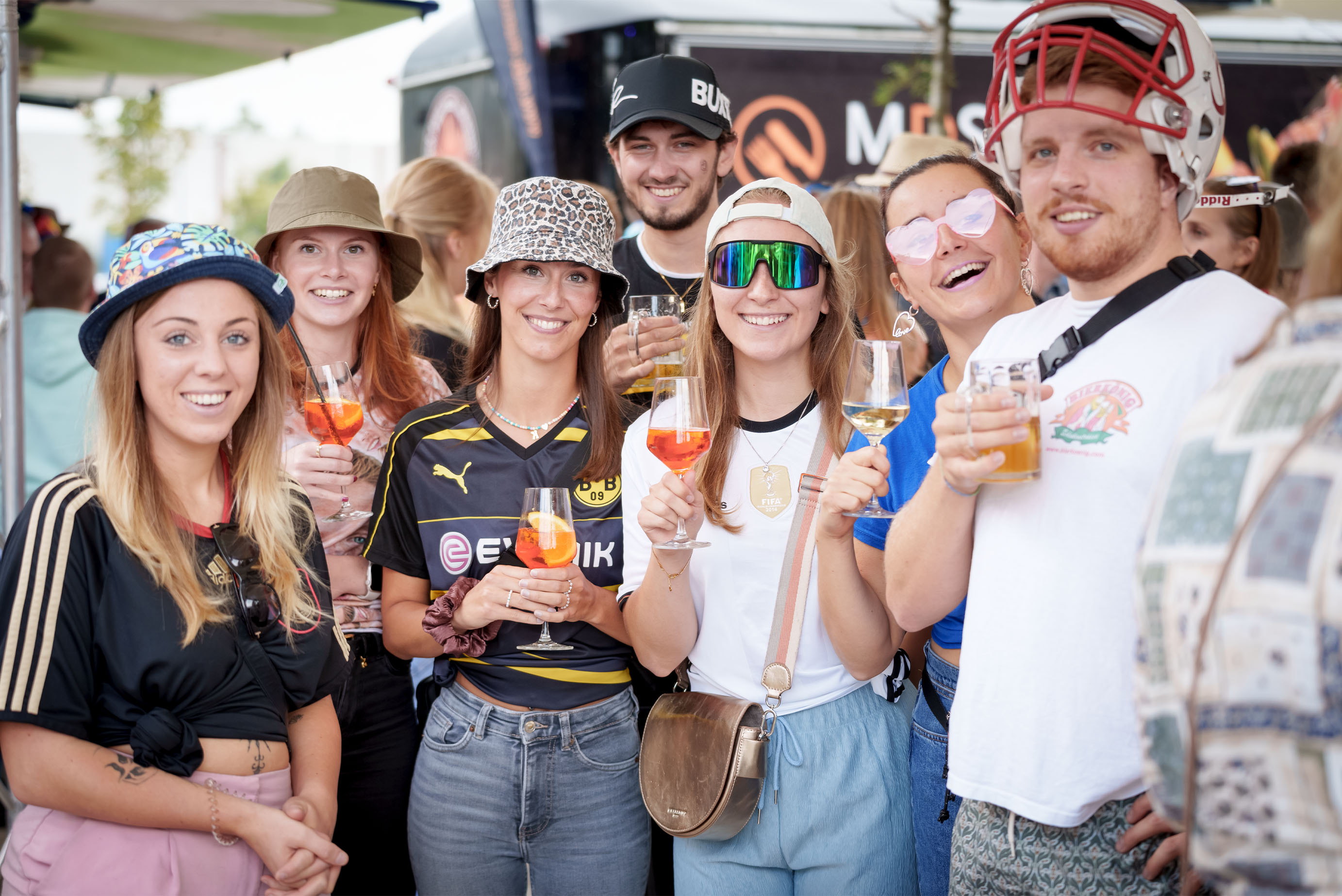 Eine Gruppe junger Menschen mit Fußballtrickots steht nebeneinander und lacht in die Kamera, alle haben einen Aperol in der Hand