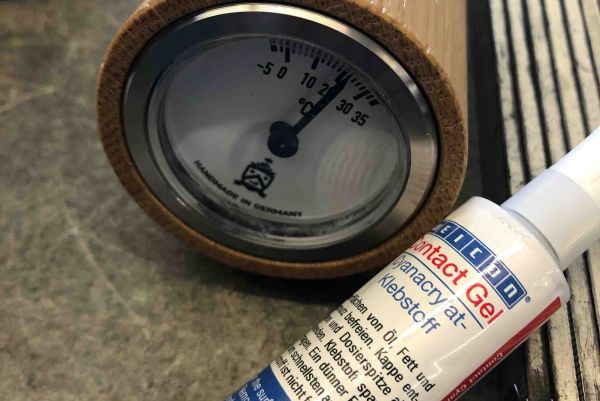 Flacon de colle WEICON Contact Gel à côté d'un thermomètre analogique encastré dans un support en bois.