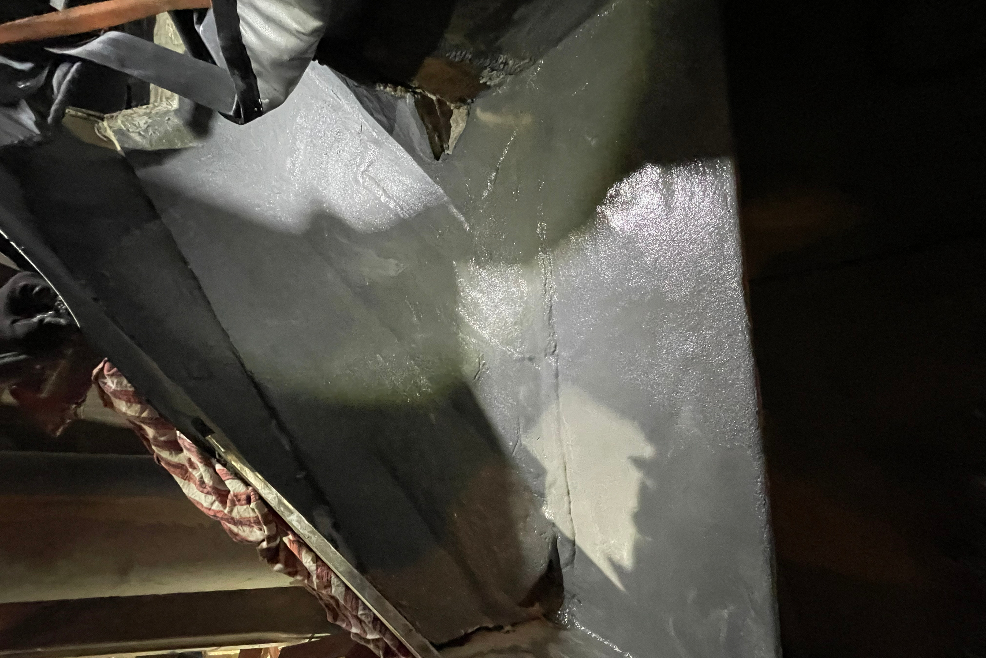 Una superficie metallica industriale interna rivestita di grigio, parzialmente illuminata da una fonte di luce durante i lavori di riparazione e rivestimento.