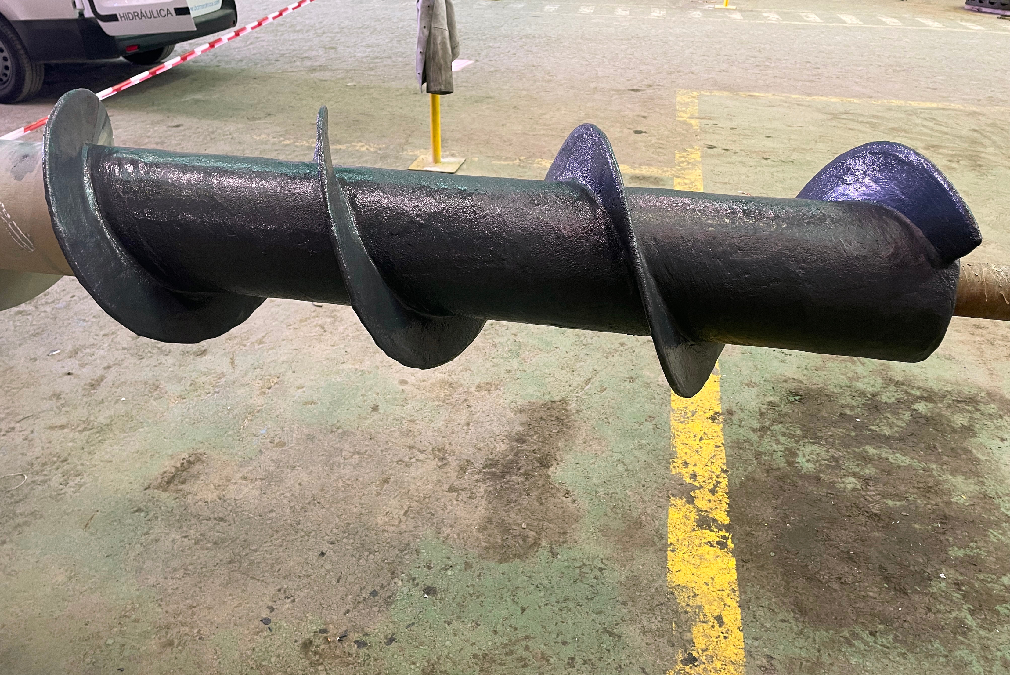 Una coclea industriale completamente rivestita e sigillata in colore nero, posizionata sul pavimento all'interno di un'officina.
