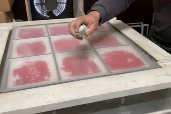 Application d'un produit en aérosol sur un écran de sérigraphie à compartiments rectangulaires par une personne.