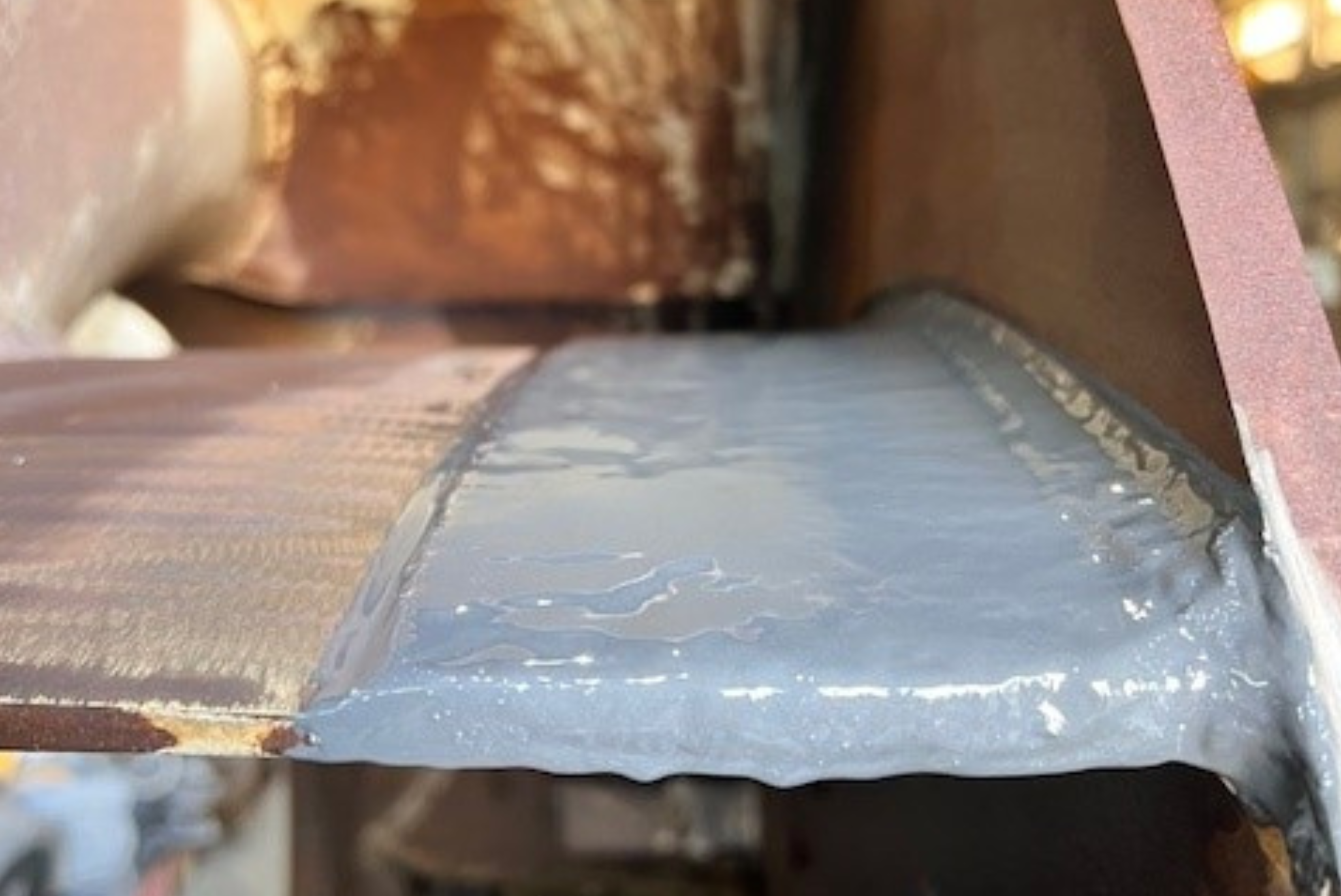 Un componente metallico industriale con un cordone di saldatura ricoperto e sigillato da uno strato di resina protettiva grigia.