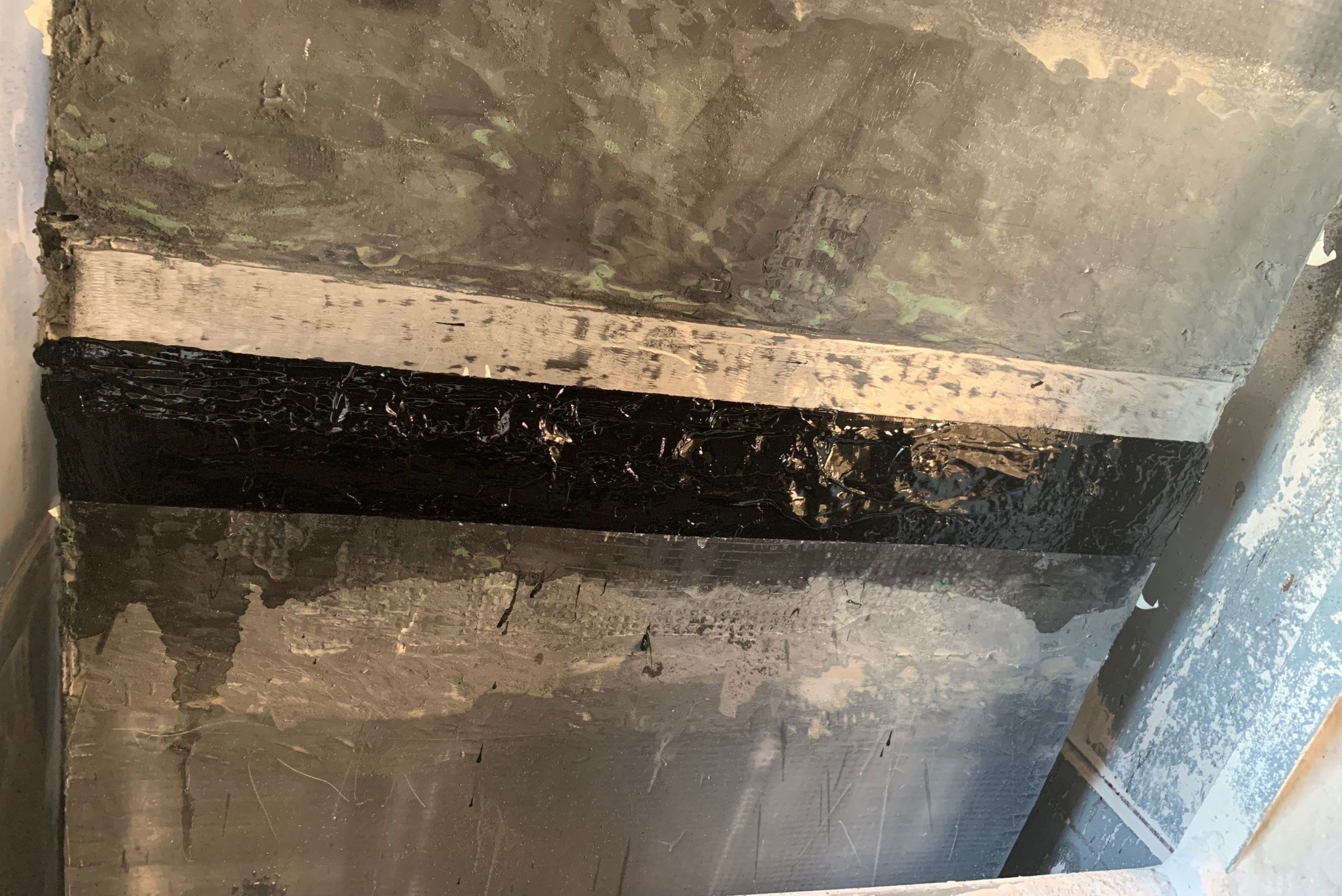 Una superficie industriale in cemento o pietra con una giunzione orizzontale marcata da una spessa striscia di sigillante nero al centro.