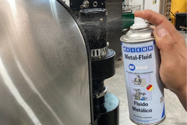 Application du produit en spray WEICON Metal-Fluid sur une surface métallique industrielle par un opérateur.