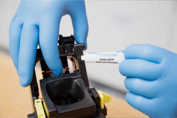 Application de graisse silicone WEICON Silikonfett sur un composant mécanique par un opérateur en gants bleus.