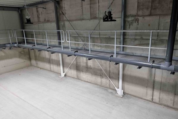 Passerelle industrielle en métal avec garde-corps fixée le long d'un mur en béton dans un local technique.