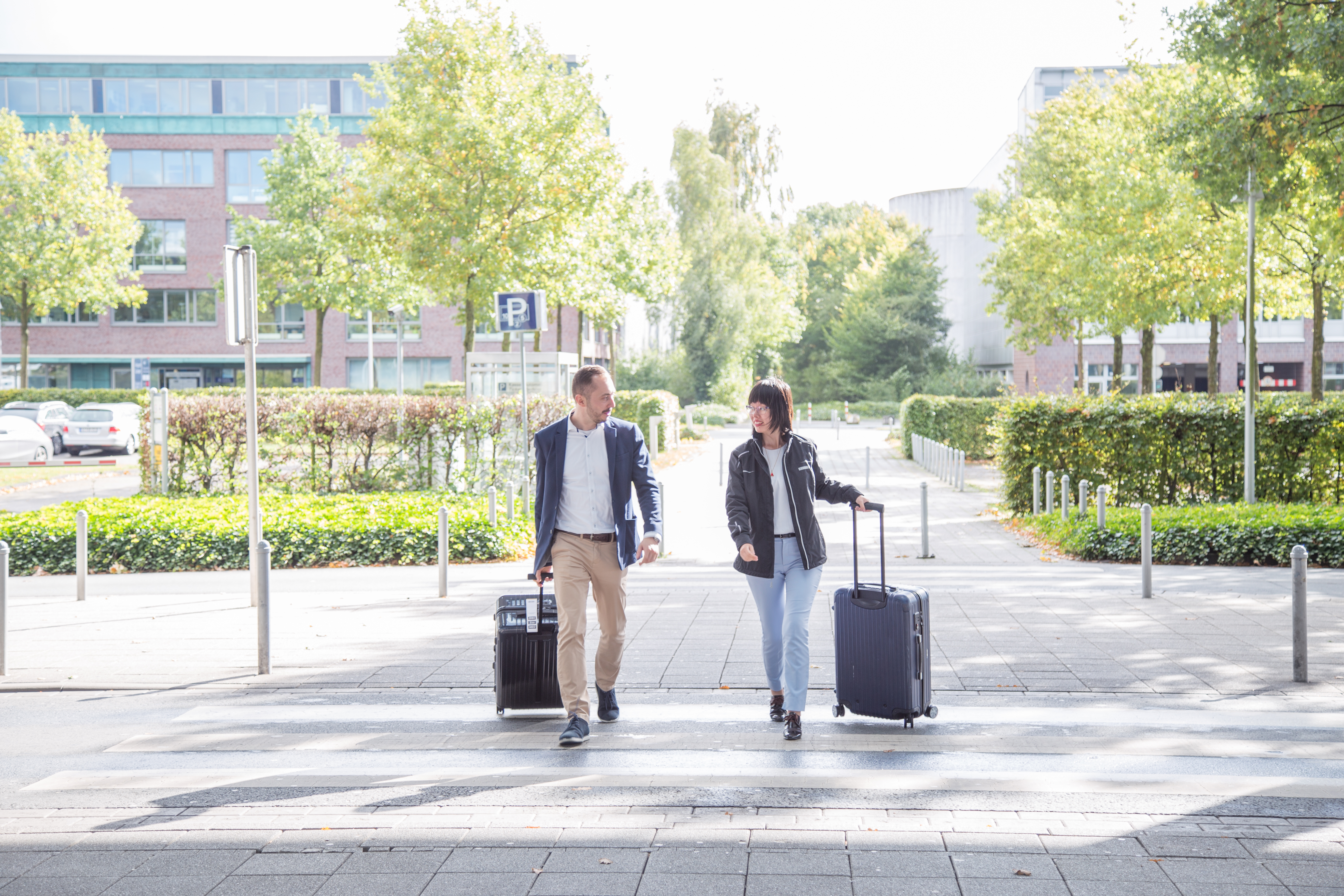 Ein Mann und eine Frau laufen mit jeweils einem Koffer in der Hand über einen Gehweg