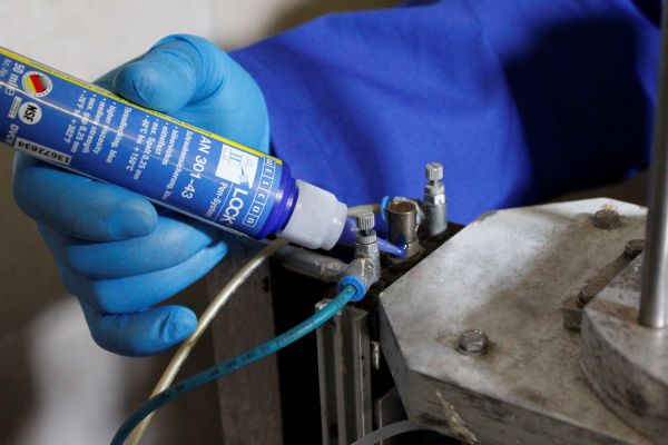 Application du freinfilet WEICONLOCK AN 301-43 sur un raccord métallique par un technicien portant des gants bleus.