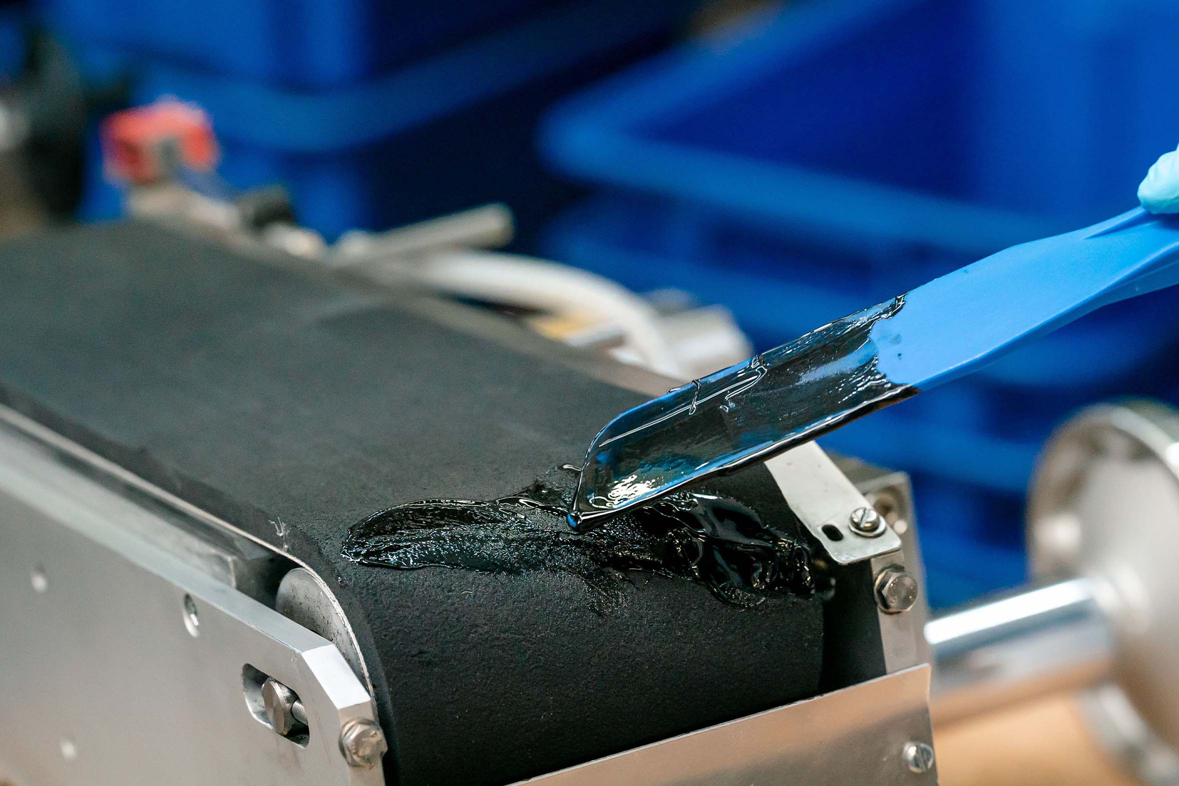 schwarze Vergussmasse wird mit einem blauen Spatel auf defektem Förderband verteilt