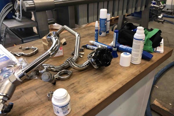 Établi en bois avec des tuyaux en acier inoxydable et plusieurs produits de maintenance WEICON posés dessus.